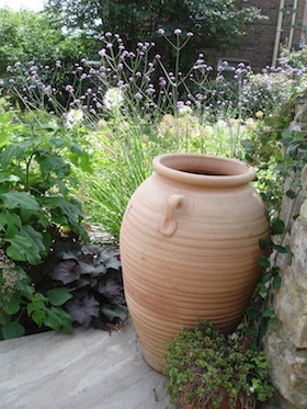 terracotta urn on terrace near stone wall with planting behind